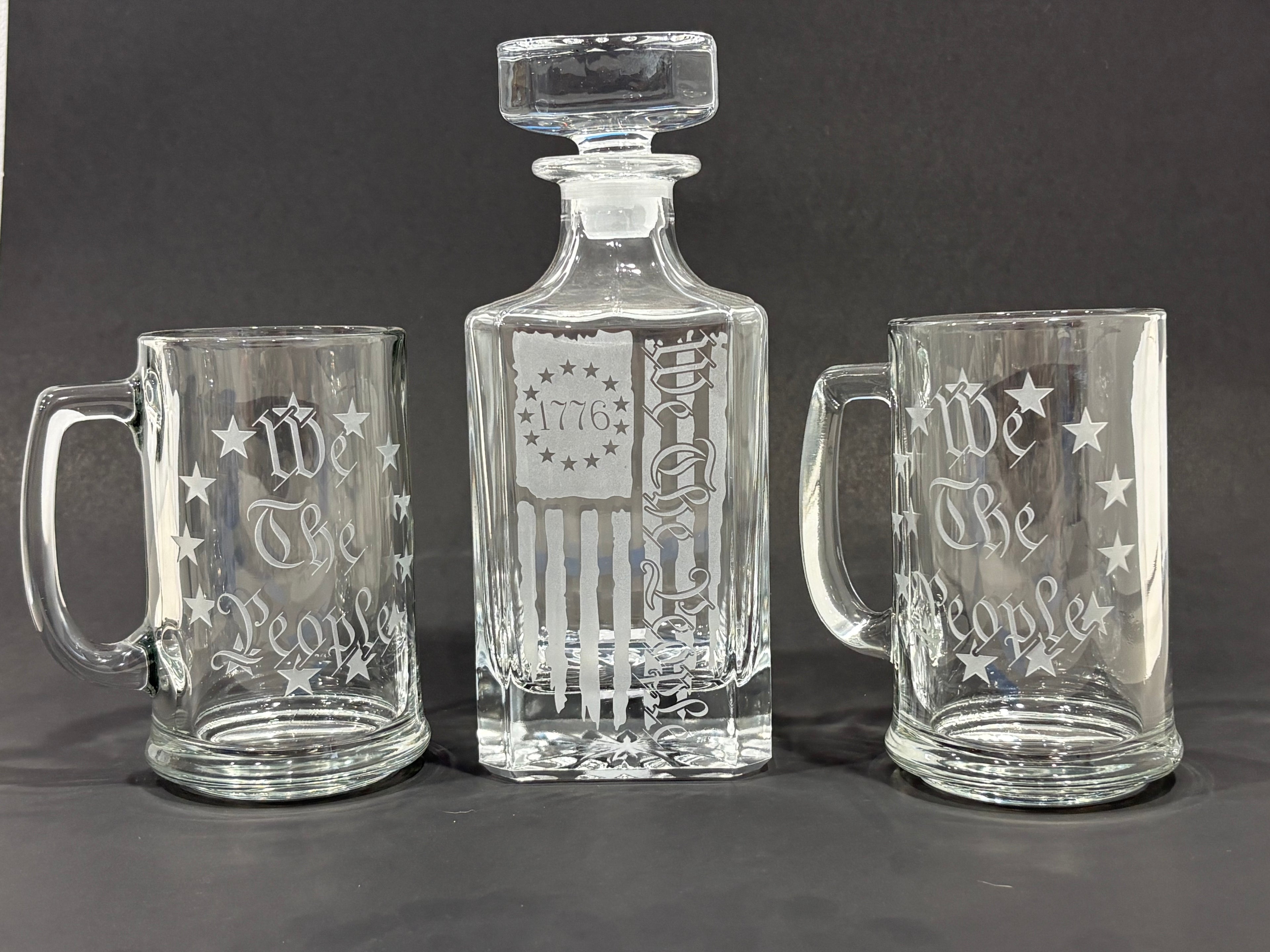 Set of glass decanter and mugs with 'We The People' engraving on a dark background